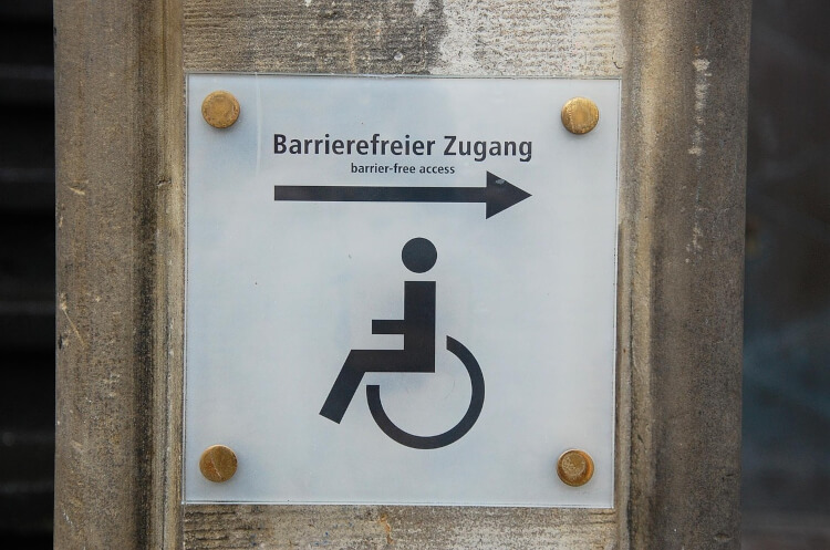Unternehmensberatung Barrierefreiheit Fallbeispiel: Hinweisschild auf barrierefreien Zugang zu einem Gebäude